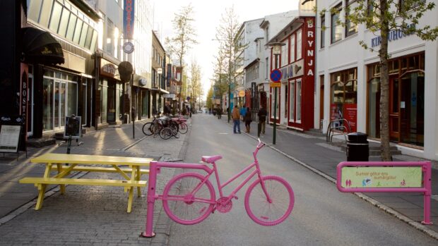 A pink bicycle sculpture on a street in Reykjavik with people walking in the background