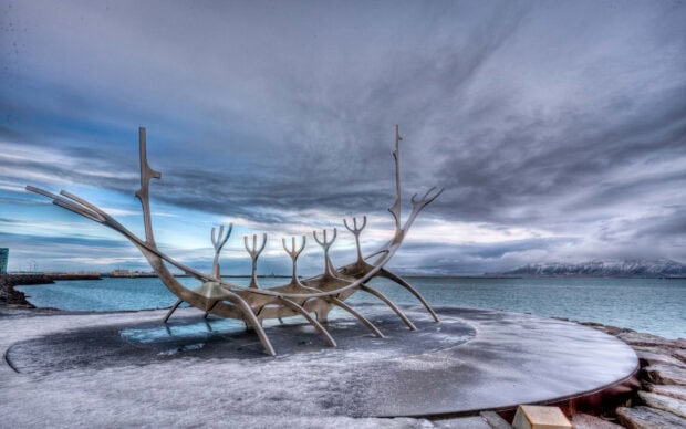 A steel sculpture of the sun voyager stands on a frozen shore in Reykjavik under a cloudy sky