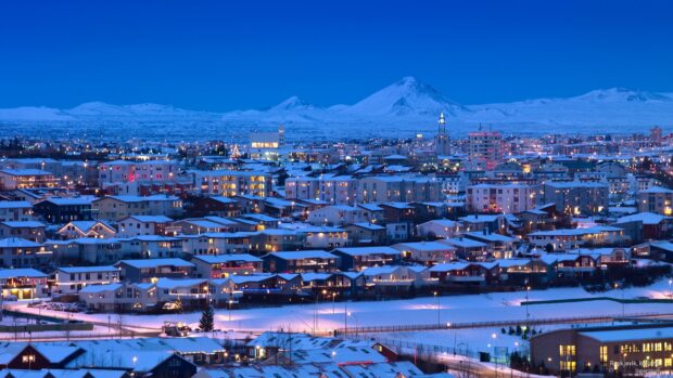 Snow covered Reykjavik cityscape with illuminated houses and mountains in the background