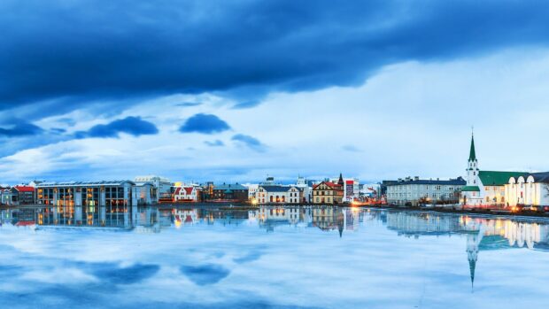 Scenic Reykjavik cityscape reflecting on calm water under blue cloudy sky