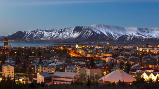 Snowy mountains overlooking Reykjavik cityscape at dusk with lit buildings and clear sky