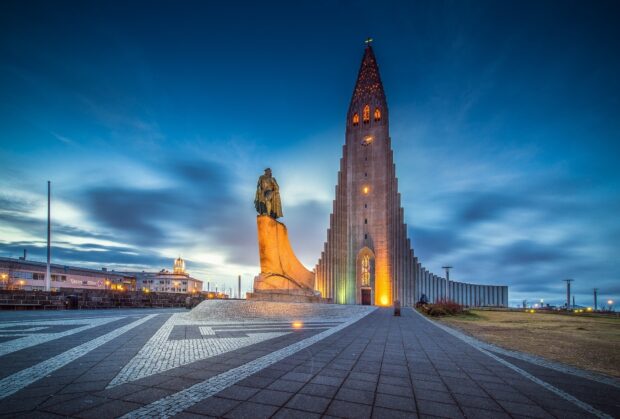 The statue of Leif Erikson in front of Hallgrimskirkja in Reykjavik at dusk with vibrant lighting and a cloudy sky