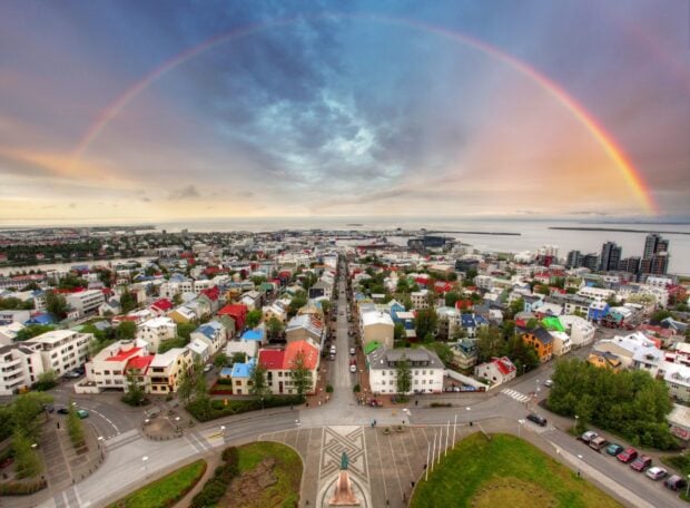 A panoramic view of Reykjavik city with colorful buildings under a vibrant rainbow