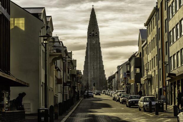 The towering church is seen from a Reykjavik street lined with parked cars and buildings