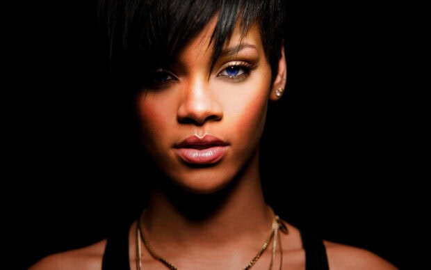 Rihanna with short hair and blue eyes in a close up portrait against a black background