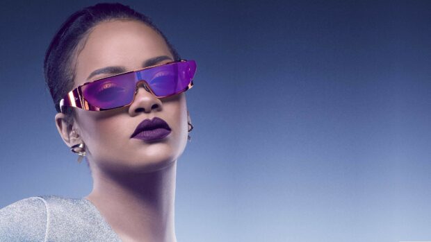Rihanna wearing purple sunglasses and bold lipstick against a blue gradient background