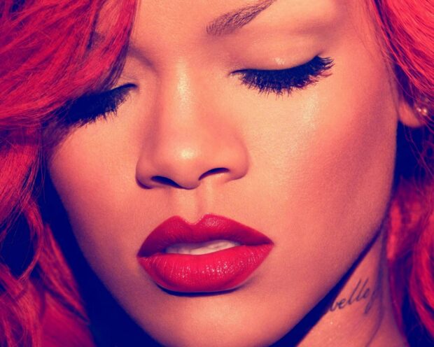 Close up of Rihanna showing her red lips and lashes with red hair and tattoo on neck