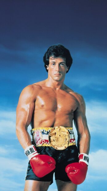 Rocky wearing red boxing gloves and a championship belt in a confident pose against a blue sky background