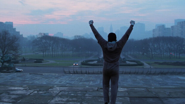 Rocky standing with raised arms overlooking cityscape on chilly morning with Rocky in focus