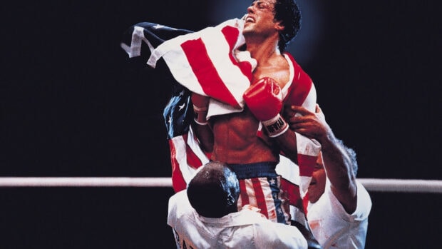 Rocky celebrates victory holding the American flag after the fight with red boxing gloves