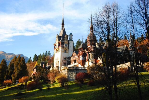 A historic Romanian castle surrounded by autumn trees and green hills on a sunny day