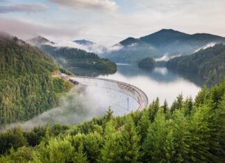 A curved dam surrounded by lush green forests and misty mountains in Romania