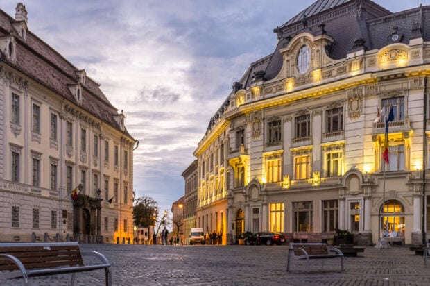 Historic architecture in Romania city street at dusk with illuminated buildings and cobblestone pavement