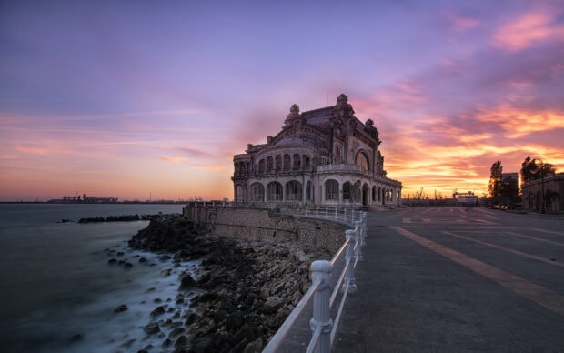 Historic Romanian building by the sea under a colorful sunset sky