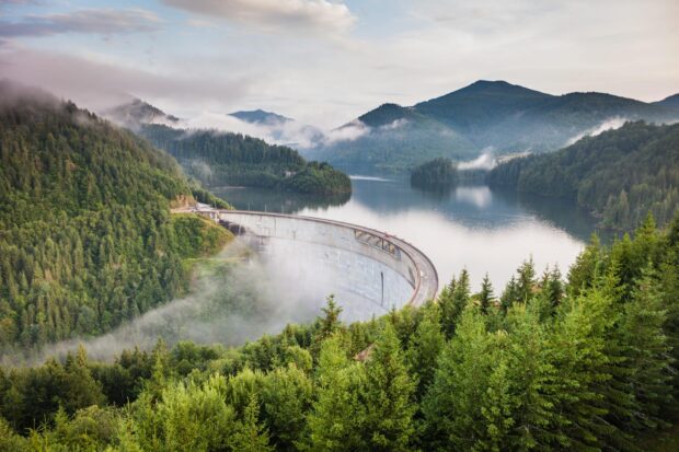 A curved dam surrounded by lush green forests and misty mountains in Romania