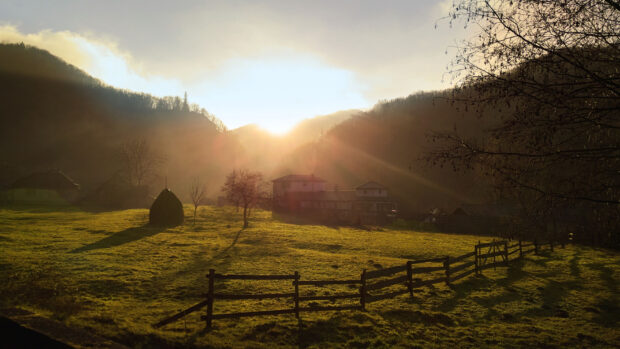 Sunrise over a peaceful Romania village with houses hills and a wooden fence