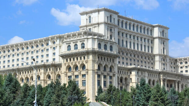 The Romania Palace of the Parliament is a monumental building surrounded by trees under a blue sky