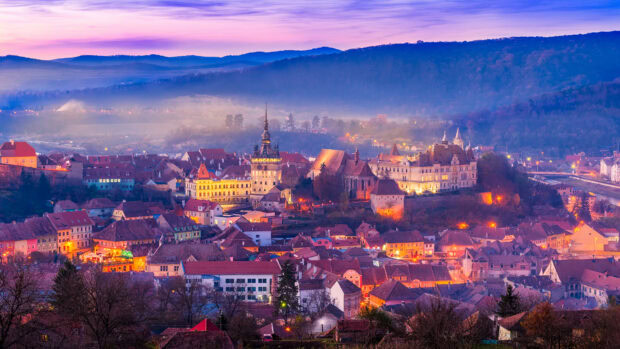A stunning view of Romania cityscape at dusk with fog and illuminated historic buildings in Romania