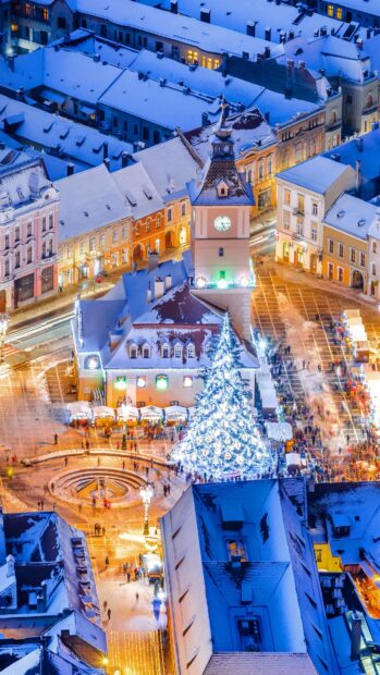 A snowy Romania city square with historic clock tower and festive Christmas tree lights