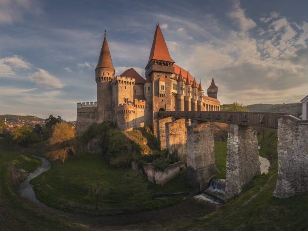 Historic Romania castle surrounded by green landscape and river under cloudy sky