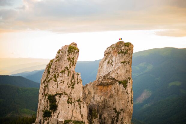 Large rock formations in Romania with the national flag on top surrounded by mountain scenery