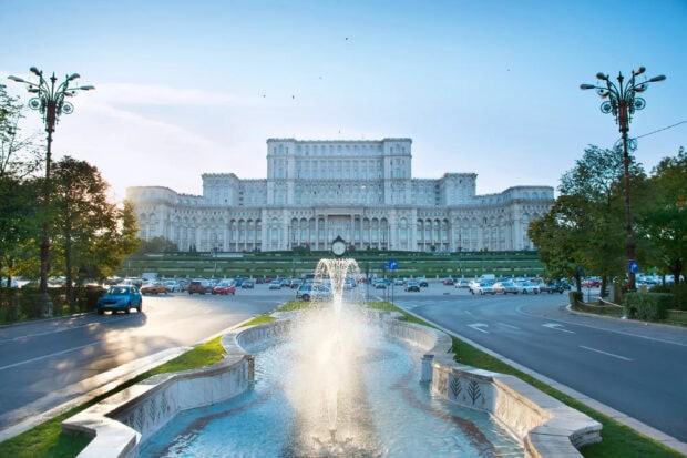 The Palace of the Parliament in Romania with a fountain and surrounding streets in clear daylight