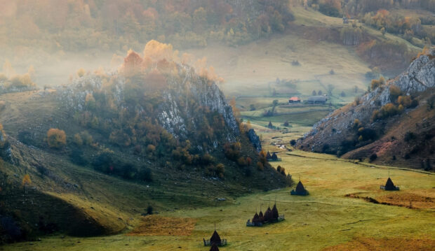 Foggy autumn landscape with rocky hills and haystacks in Romania valley