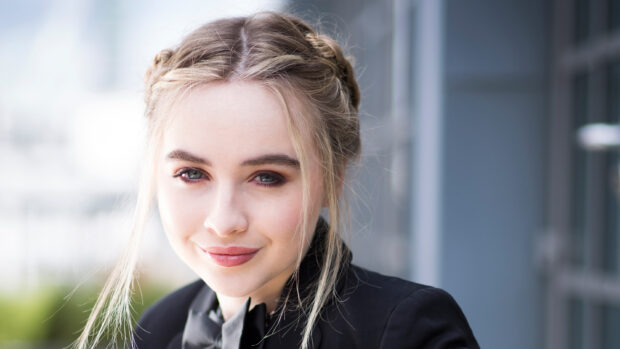 Sabrina Carpenter wearing a black blazer smiling softly with braided hair outdoors