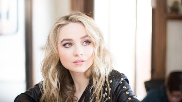 Sabrina Carpenter looking thoughtfully to the side with wavy blonde hair and a studded black leather jacket
