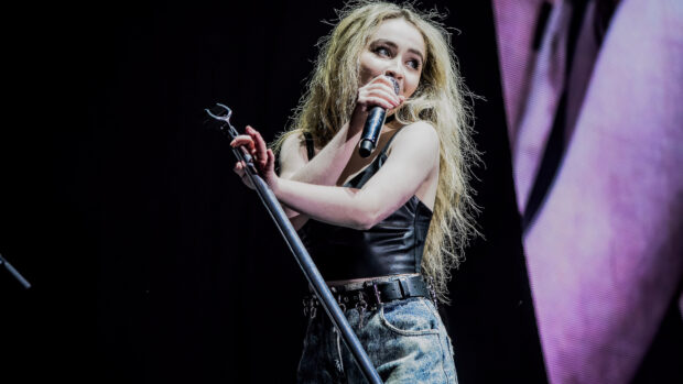 Sabrina Carpenter performing live on stage holding a microphone with a leather top and denim jeans