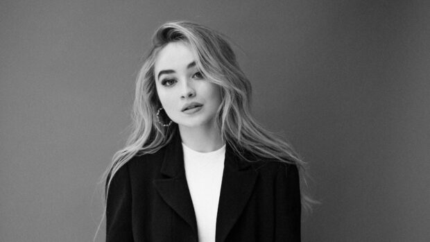 Sabrina Carpenter posing in a black jacket and white top with long hair flowing naturally