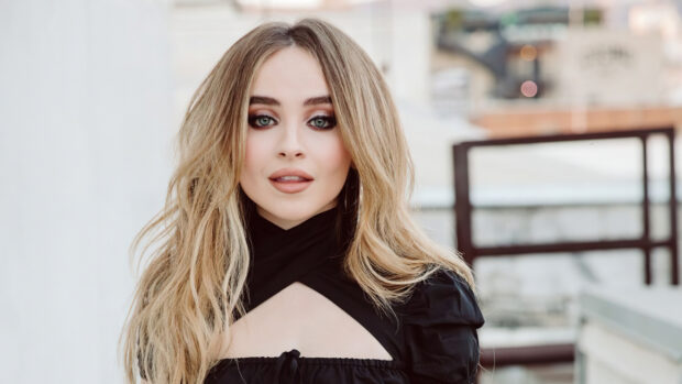 Sabrina Carpenter with long blonde hair wearing a black top looking at the camera