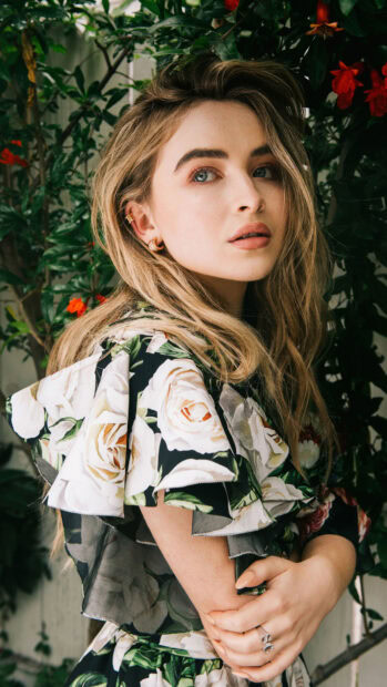 Sabrina Carpenter wearing a floral dress posing outdoors with greenery in the background