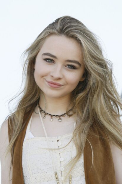 Sabrina Carpenter wearing a brown vest and a cream lace top with a beaded necklace