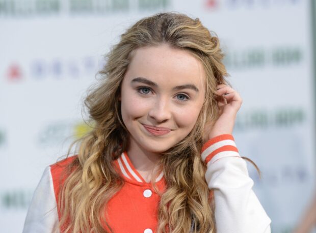 Sabrina Carpenter smiling with long curly hair and a red varsity jacket