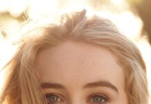 Sabrina Carpenter with long blonde hair and a bracelet looking thoughtfully into the camera