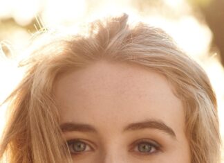 Sabrina Carpenter with long blonde hair and a bracelet looking thoughtfully into the camera