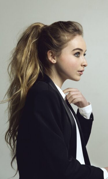 Sabrina Carpenter with long hair in a black jacket looking to the side