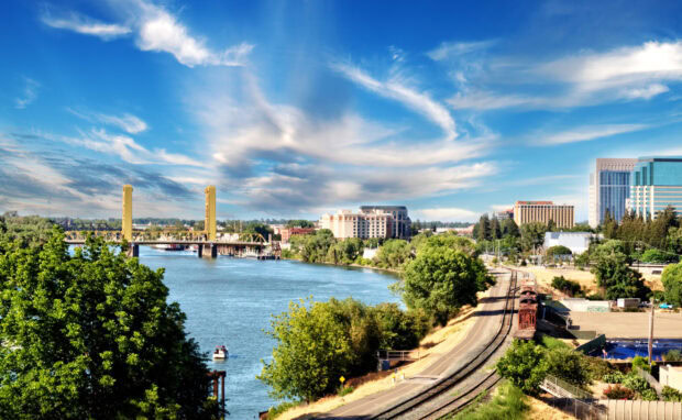 Sacramento city skyline with river forest and bridge under blue sky