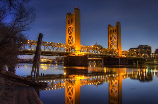 Tower bridge in Sacramento reflecting on the calm river at dusk with city lights illuminating the scene