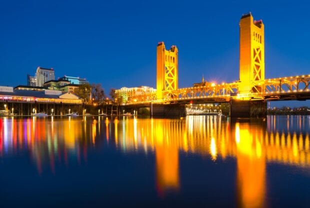 Tower Bridge in Sacramento reflecting on calm river at night with city skyline