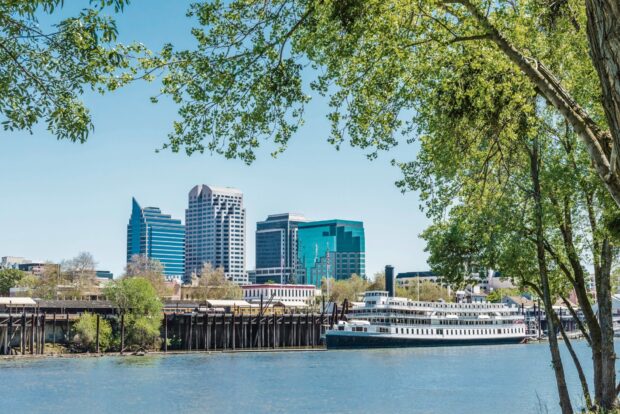 River view with Sacramento skyline and boat framed by green trees