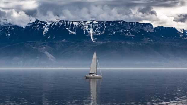 A sail boat sailing on calm water with snowy mountains in the background