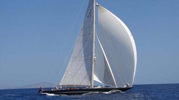 A sail boat sailing on the ocean with full white sails and clear blue sky