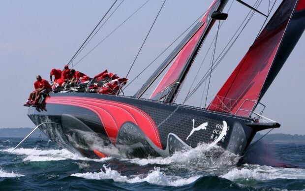 A sail boat with red and black design racing on the ocean with crew members sitting on the edge