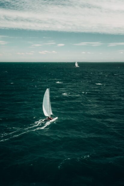 A sail boat cruising on the deep blue ocean under a partly cloudy sky