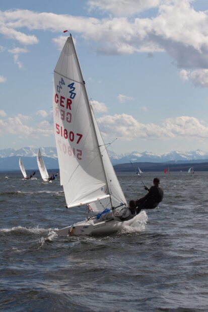 Two sailors navigating a sail boat on choppy water with mountains in the background