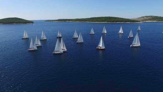 A fleet of sail boats sailing on deep blue sea near green islands