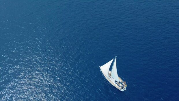 White sails of a sail boat gliding across deep blue ocean waters