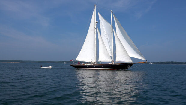 A sail boat with white sails glides smoothly across the calm blue sea